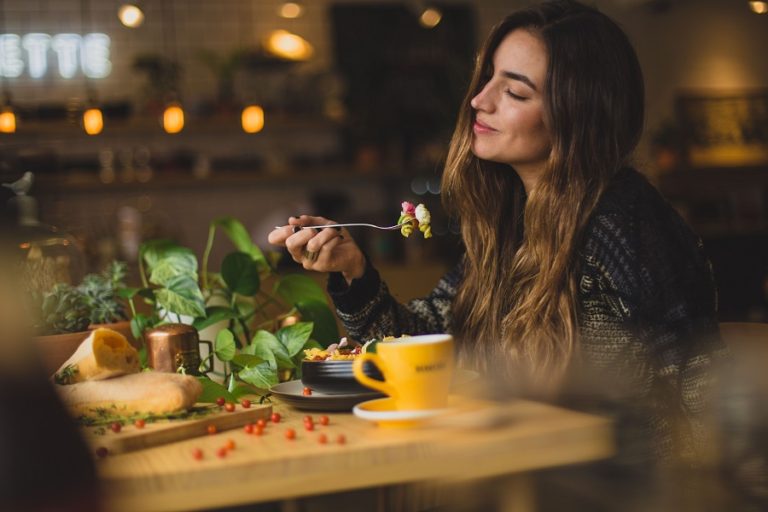 Mulher sentada em frente a uma mesa com plantas, plena ao alimentar-se, ilustrando uma rotina de alimentação ayurvédica