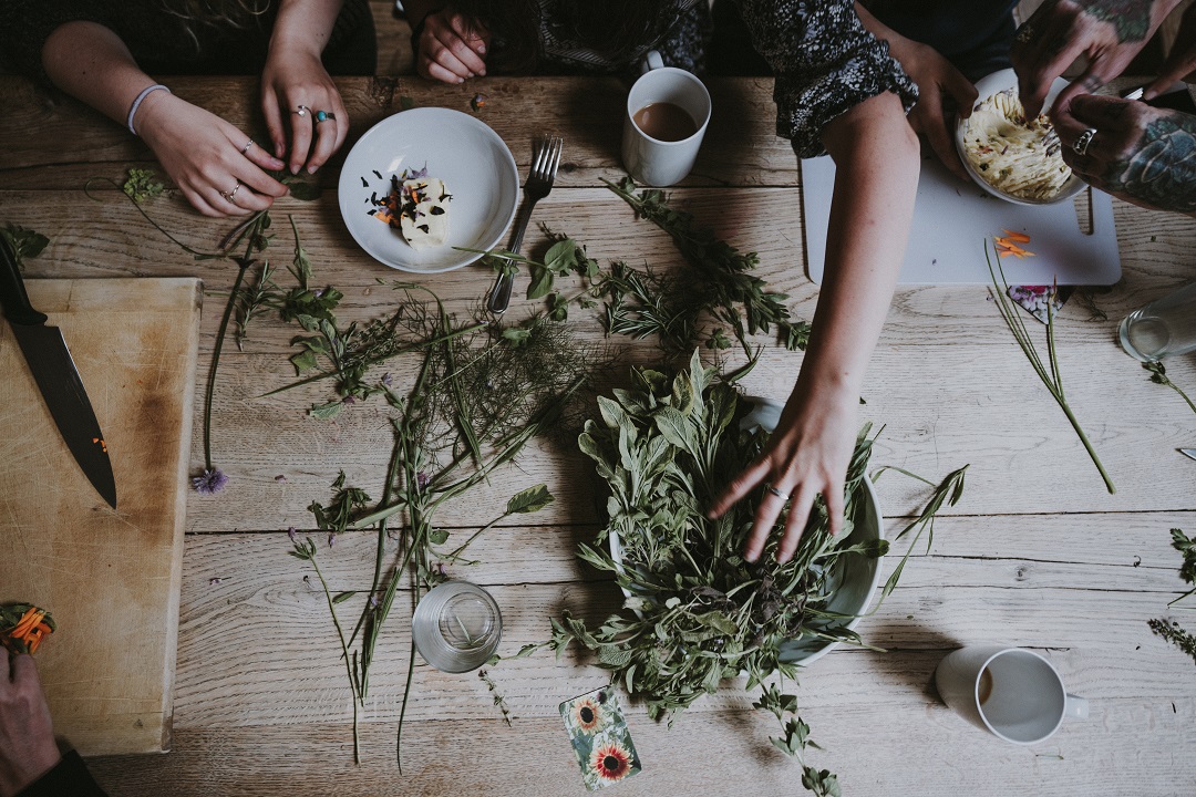 Dicas de especiarias: mesa de madeira cheia de ervas e especiarias e mãos de diferentes pessoas manuseando as ervas