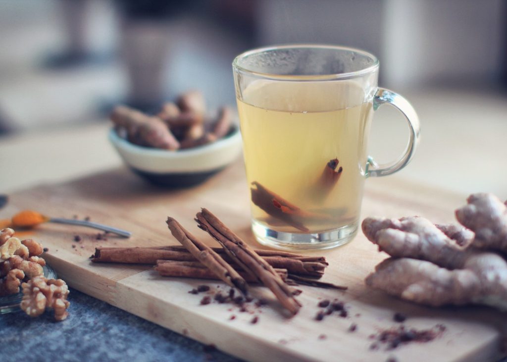 dicas de especiarias: imagem de uma xícara de chá de canela em cima de uma tábua de madeira decorada com vários paus de canela