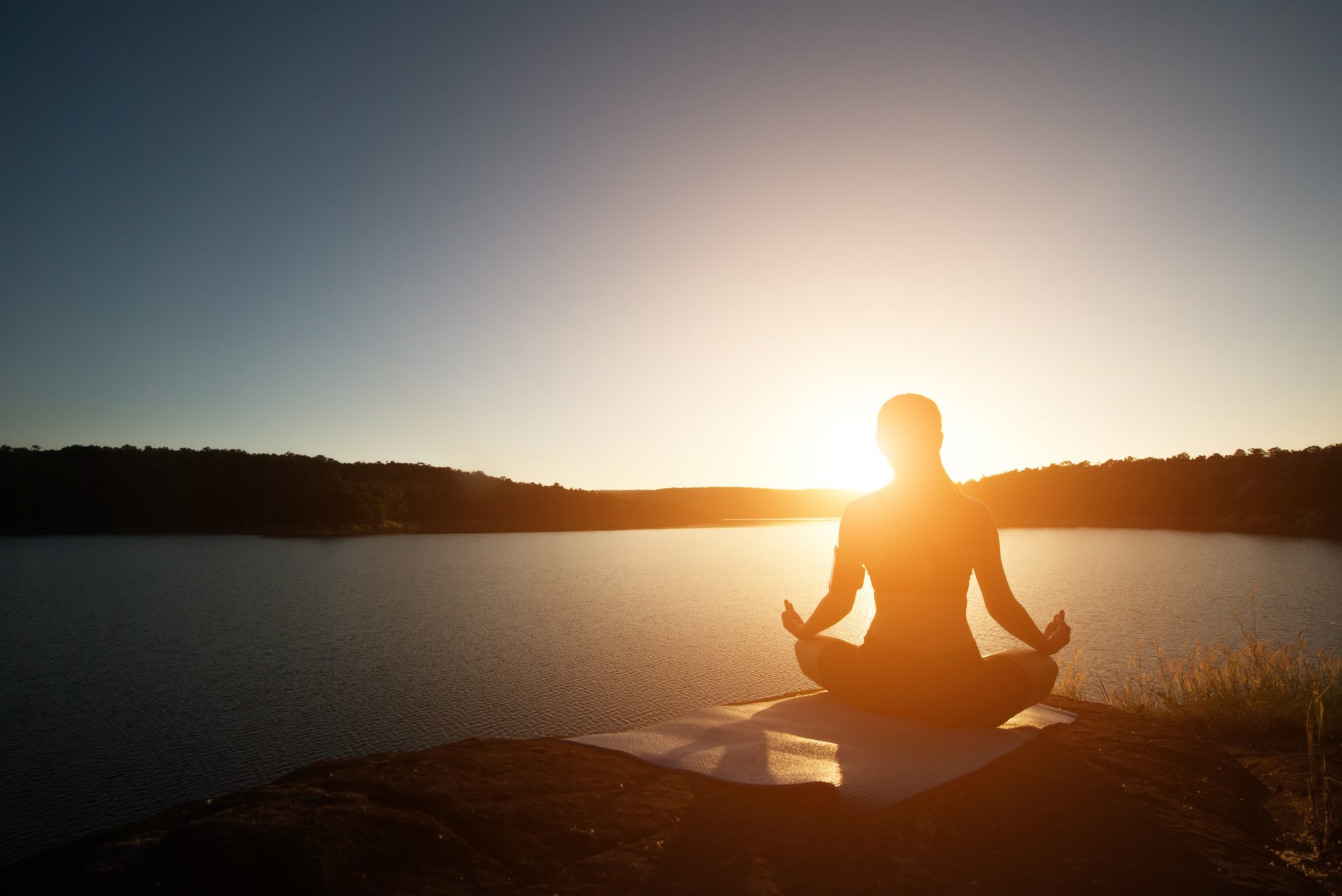 detox de Outono: Mulher meditando sentada em uma pedra de frente a um lago ao por do sol